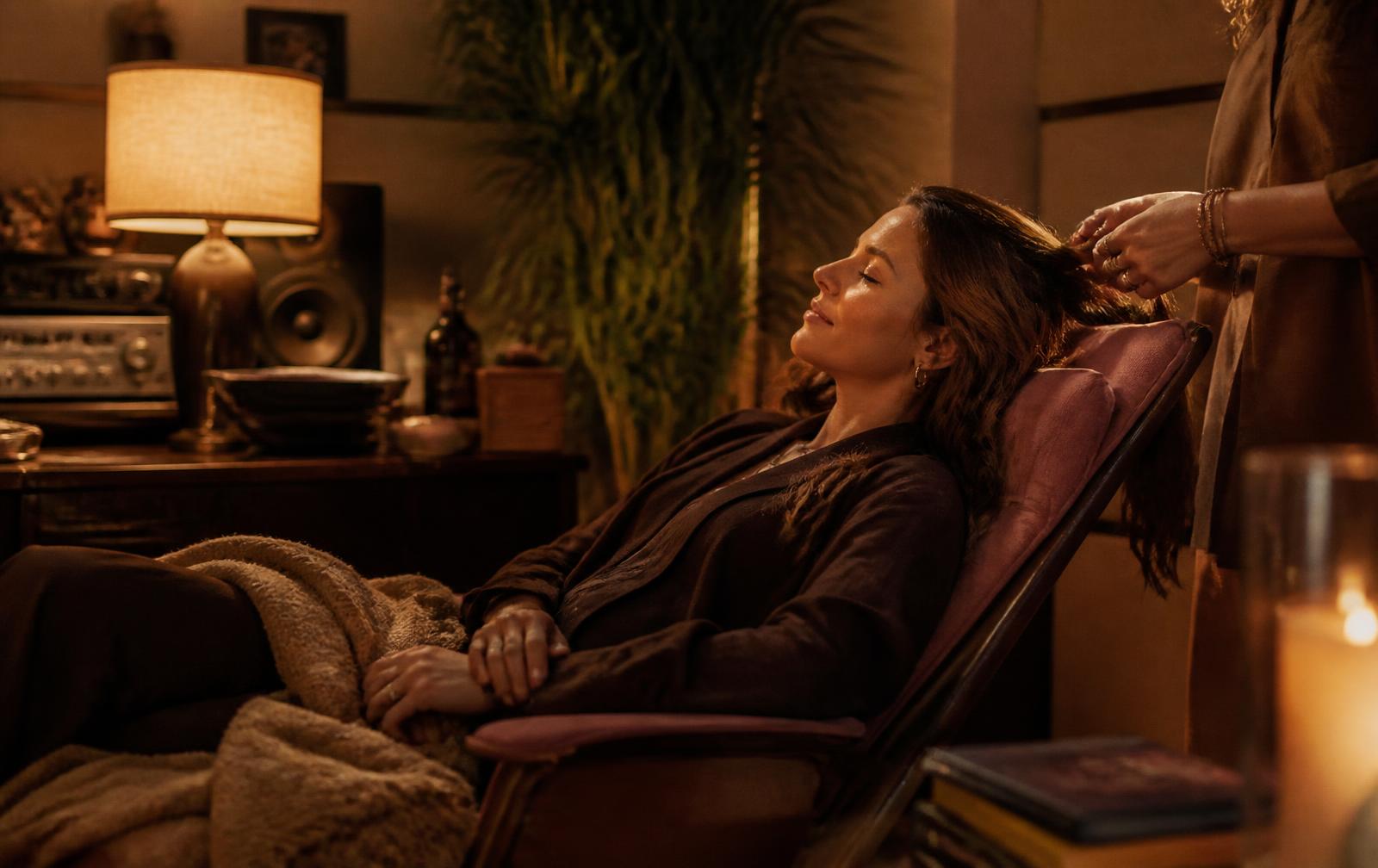 A fully clothed guest resting in a warmly lit Laurel Canyon room while their hair is gently played with
